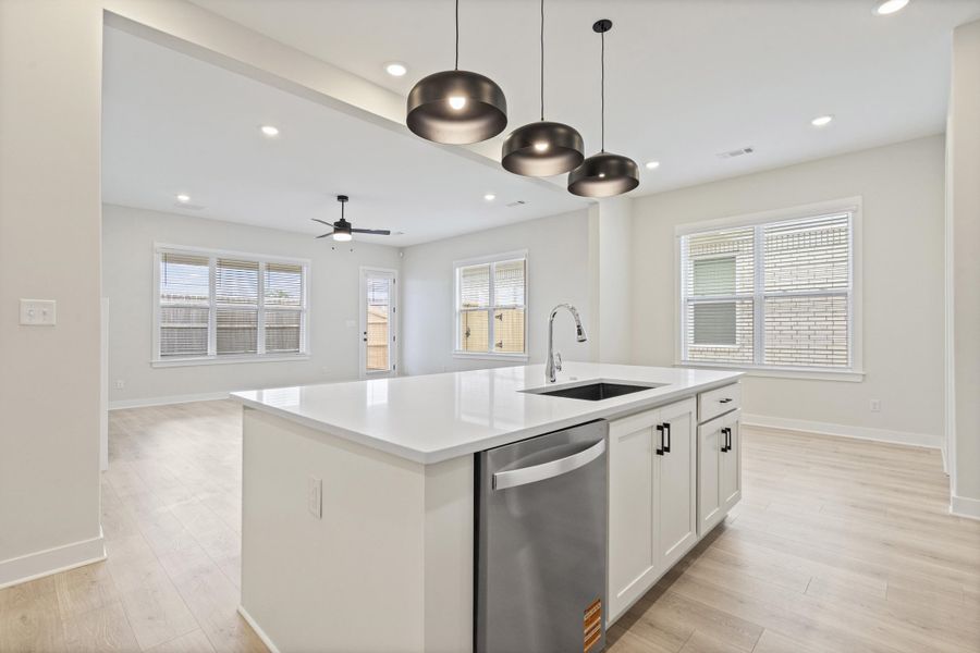 Kitchen island featuring a white countertop, stainless steel sink, pull-down faucet, and integrated dishwasher Kitchen island featuring a white countertop, stainless steel sink, pull-down faucet, and integrated dishwasher