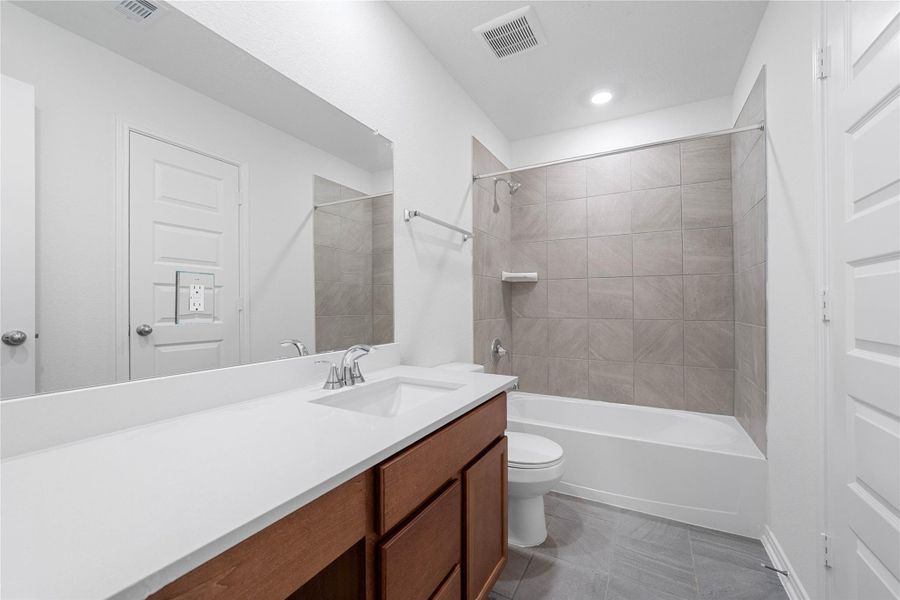 The secondary bathroom showcases tile flooring, a bath/shower combo with Daltile tile surround, a vanity with knee space and a stunning light countertop, large mirror, sleek fixtures, and contemporary finishes throughout. The secondary bathroom showcases tile flooring, a bath/shower combo with Daltile tile surround, a vanity with knee space and a stunning light countertop, large mirror, sleek fixtures, and contemporary finishes throughout.