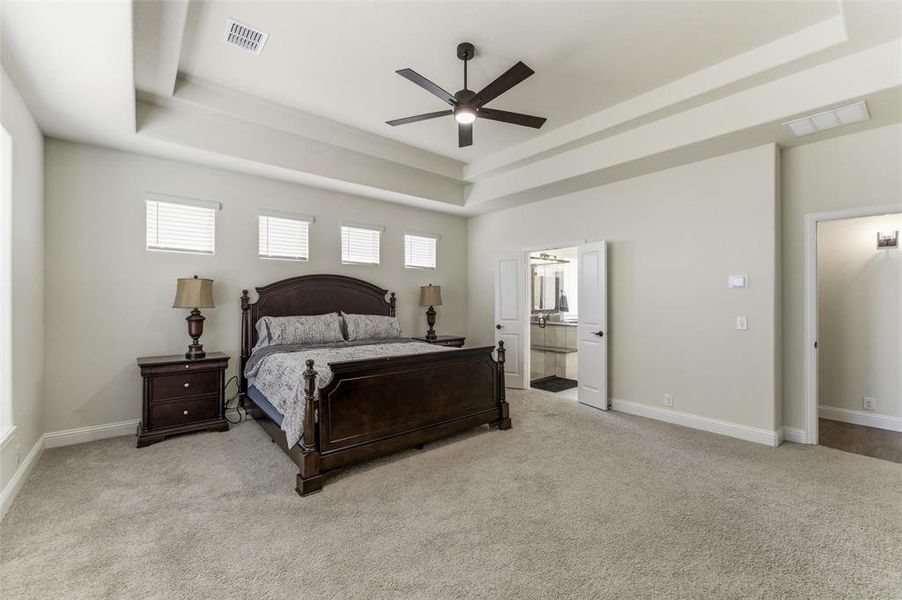Bedroom featuring a tray ceiling, light colored carpet, ceiling fan, and ensuite bath