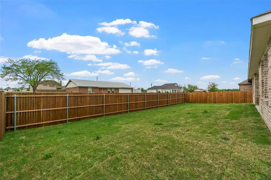 Expansive backyard featuring a wood privacy fence, green lawn, and brick exterior