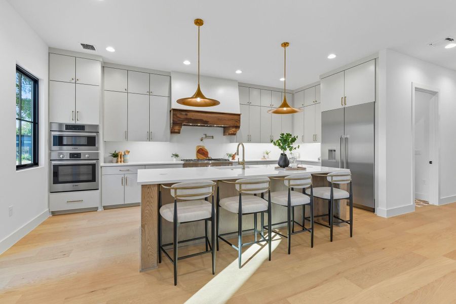 Kitchen with a kitchen breakfast bar, a center island with sink, built in refrigerator, decorative light fixtures, and light wood-style floors Kitchen with a kitchen breakfast bar, a center island with sink, built in refrigerator, decorative light fixtures, and light wood-style floors