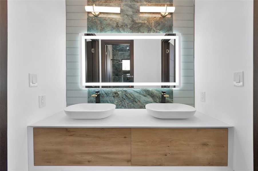 Luxurious and modern bathroom featuring dual vessel sinks, elegant wood accents, and a sleek backlit mirror.