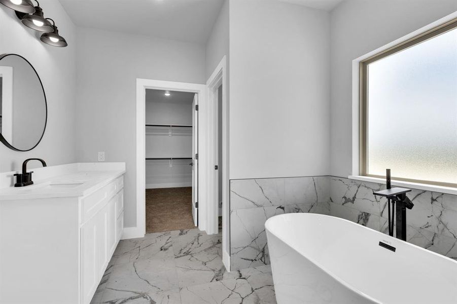 Bathroom featuring vanity, a walk in closet, light marble finish floors, a soaking tub, and tile walls