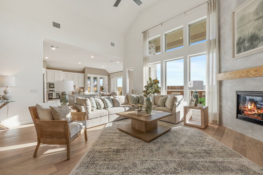 Open-concept living room with vaulted ceiling, fireplace, hardwood floors, and kitchen visible in background