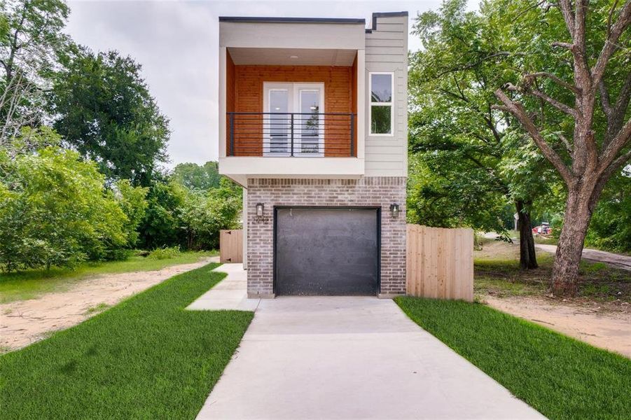 Modern home featuring a balcony, brick siding, driveway, and an attached garage