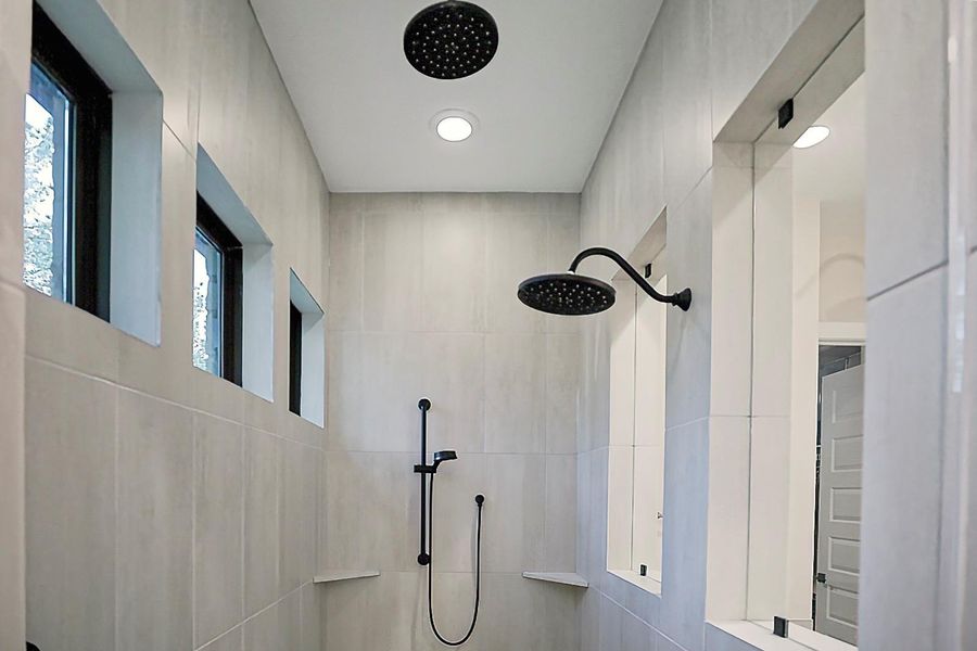 Luxurious walk-in shower with large block tiles to the ceiling, triple black matte shower heads, to include two rain shower heads.