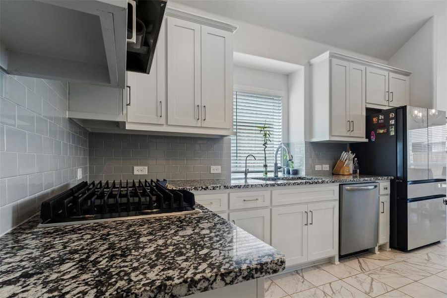 Kitchen featuring dark stone countertops, light marble finish floors, and white cabinetry