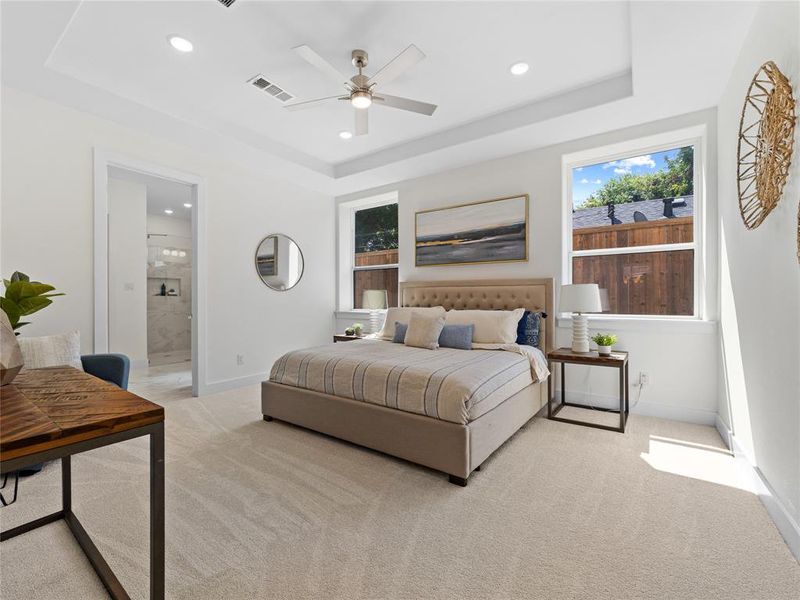 Carpeted bedroom with a raised ceiling, multiple windows, recessed lighting, ensuite bath, and ceiling fan