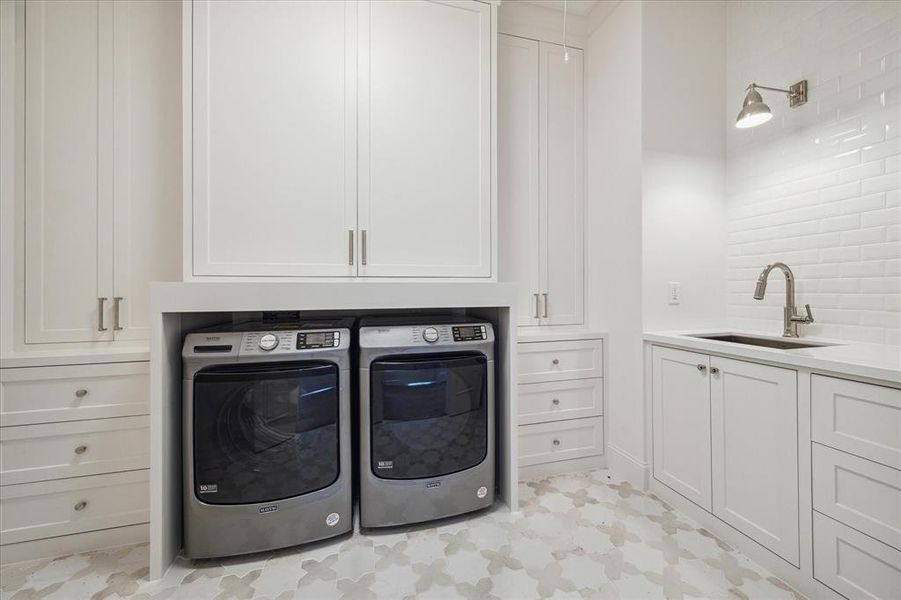 This luxurious utility room features designer floor and wall tile accents that elevate the space with style. Equipped with a Maytag washer and dryer, it also offers ample cabinetry and drawers for convenient storage and organization.