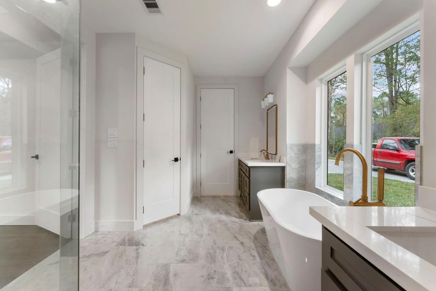 Another view to show off the freestanding tub, picture windows offering plenty of natural light, a sleek vanity with a mirror, and a spacious glass shower. The light tile flooring and neutral walls create an airy and elegant atmosphere. This en-suite features two closets