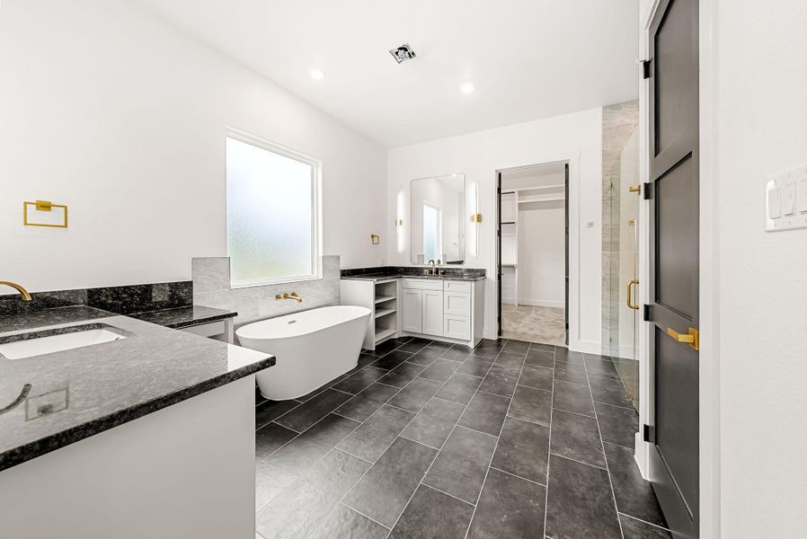 A well-appointed primary bath features dual granite-topped vanities, a luxurious soaking tub, and a spacious walk-in closet.