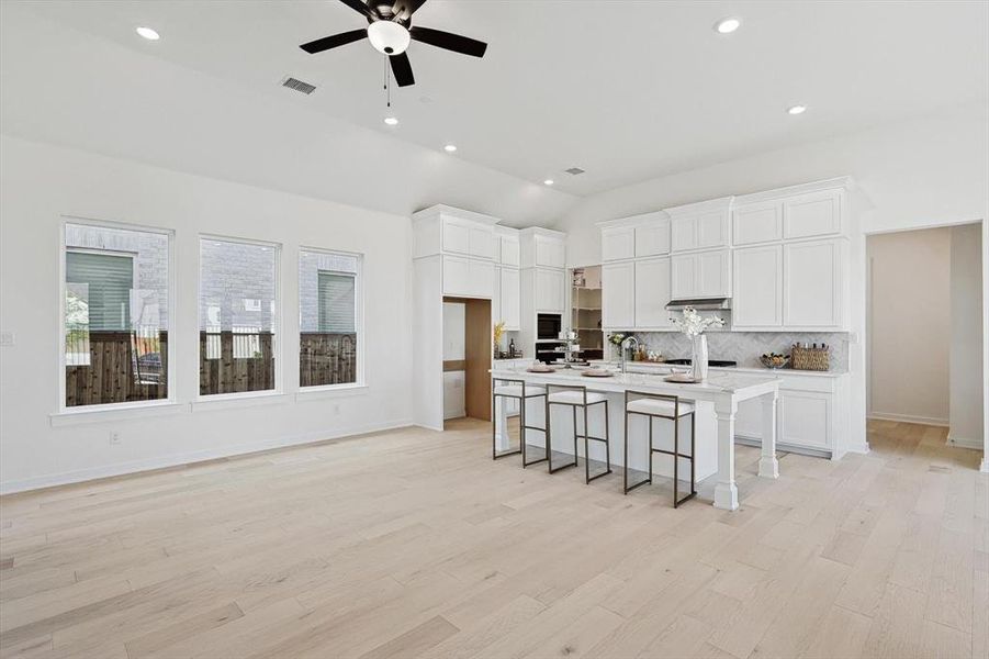 Kitchen with white cabinetry, a breakfast bar area, light hardwood / wood-style flooring, and an island with sink