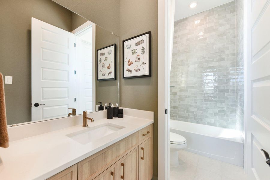 Modern stone counters and custom cabinetry anchor this well-appointed bathroom with a tiled shower tub combo.