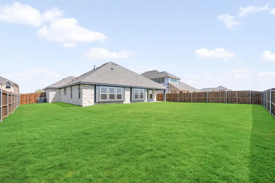 Rear view of single-story brick home with large fenced backyard and green lawn