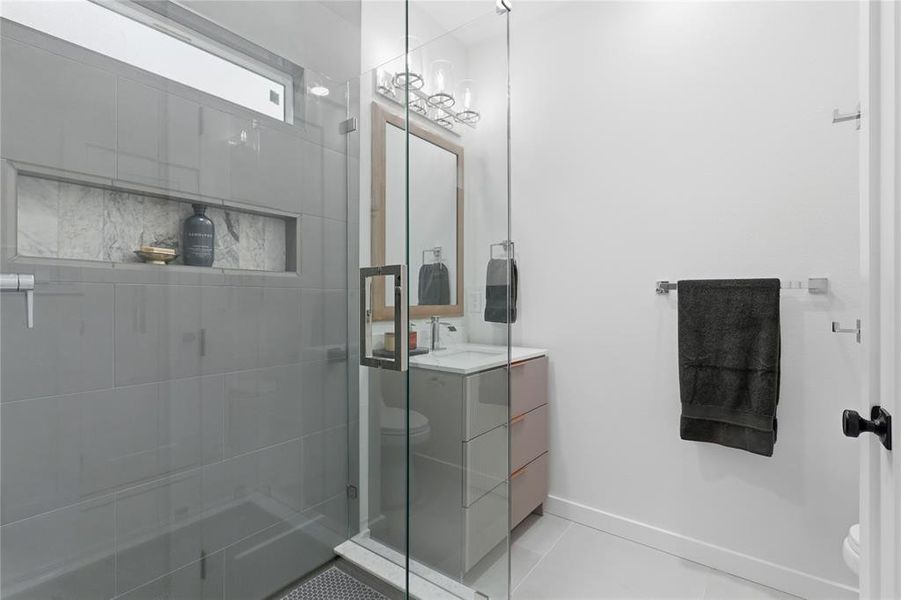 Glass-enclosed shower with gray tile surround and integrated marble-finish niche