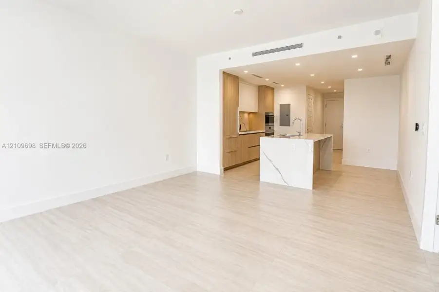 Open-concept kitchen featuring flat-panel wood-finish cabinetry, a waterfall-edge stone island, built-in appliances, recessed lighting, and wood-finish flooring