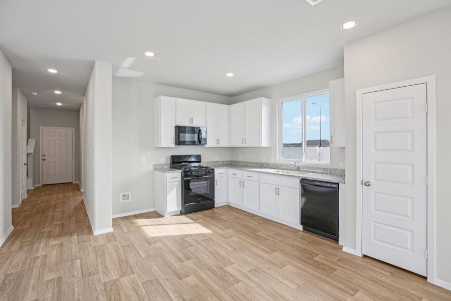 Image of a L-shaped kitchen with white cabinets, granite countertops, black appliances and a window above the sink Image of a L-shaped kitchen with white cabinets, granite countertops, black appliances and a window above the sink