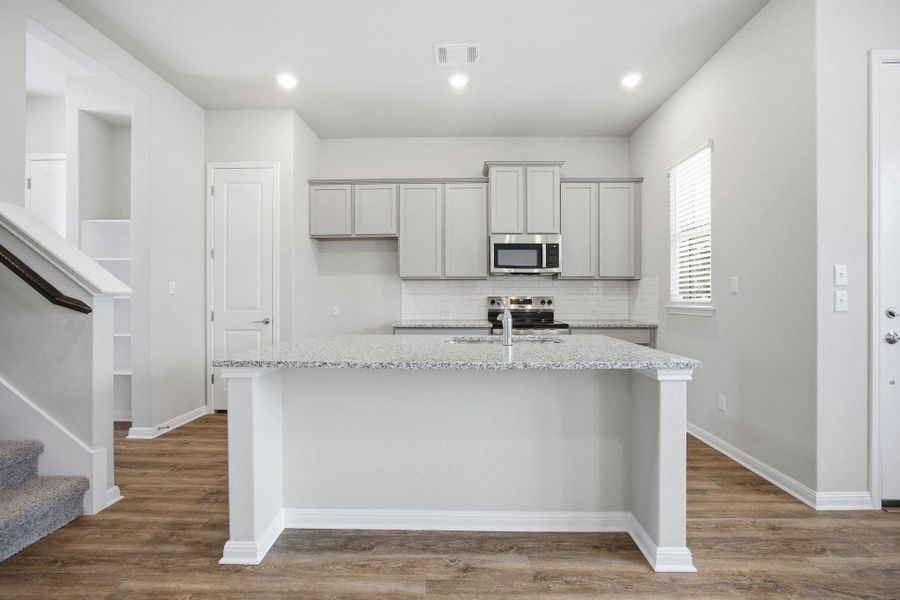 Kitchen featuring gray cabinetry, light stone countertops, stainless steel appliances, backsplash, and light wood-type flooring