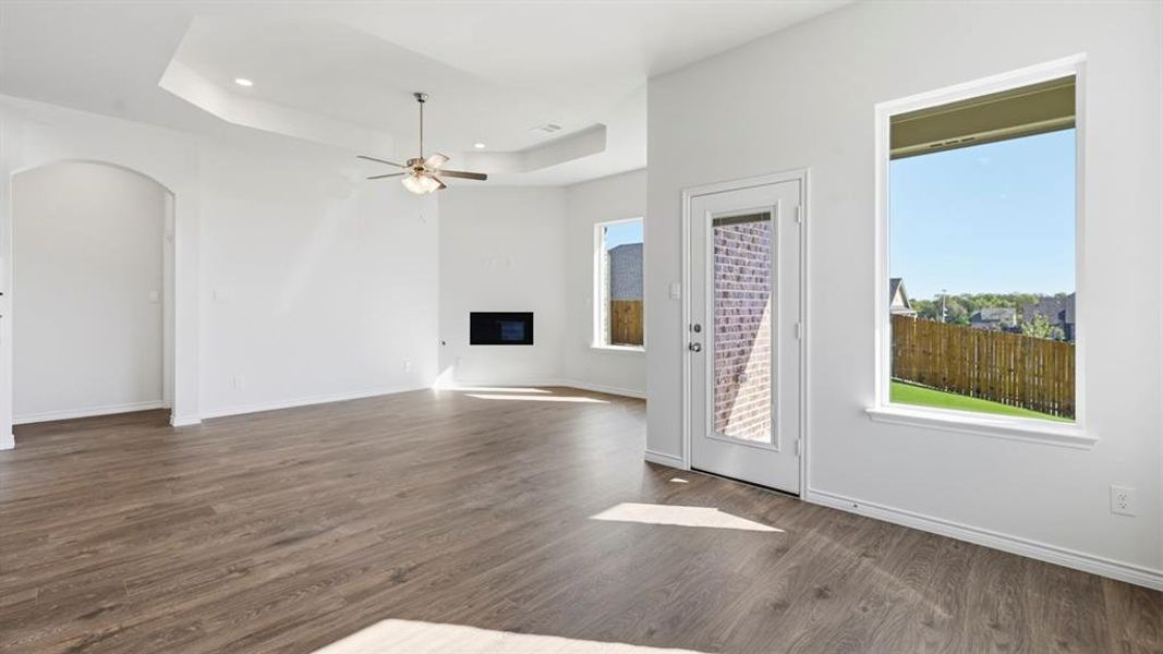 Unfurnished living room with a tray ceiling, a glass covered fireplace, dark wood finished floors, arched walkways, and a ceiling fan Unfurnished living room with a tray ceiling, a glass covered fireplace, dark wood finished floors, arched walkways, and a ceiling fan