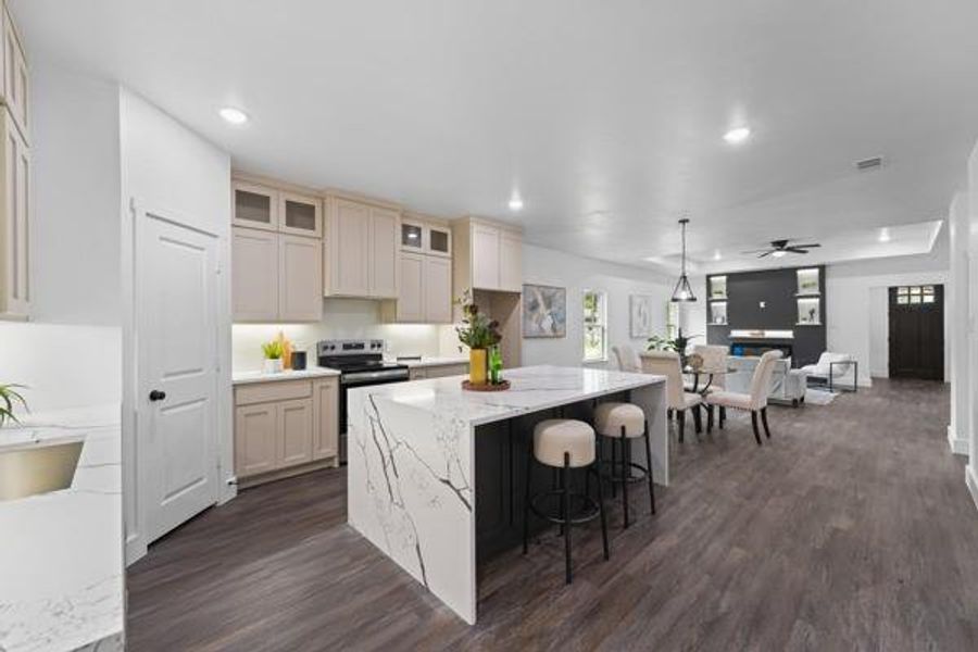 Open-concept kitchen featuring a waterfall island with stone countertop, stainless steel appliances, upper cabinetry with glass inserts, and wood-finish flooring throughout Open-concept kitchen featuring a waterfall island with stone countertop, stainless steel appliances, upper cabinetry with glass inserts, and wood-finish flooring throughout