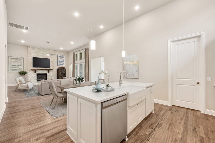 Open-concept kitchen with white island, farmhouse sink, and living room with stone fireplace in background