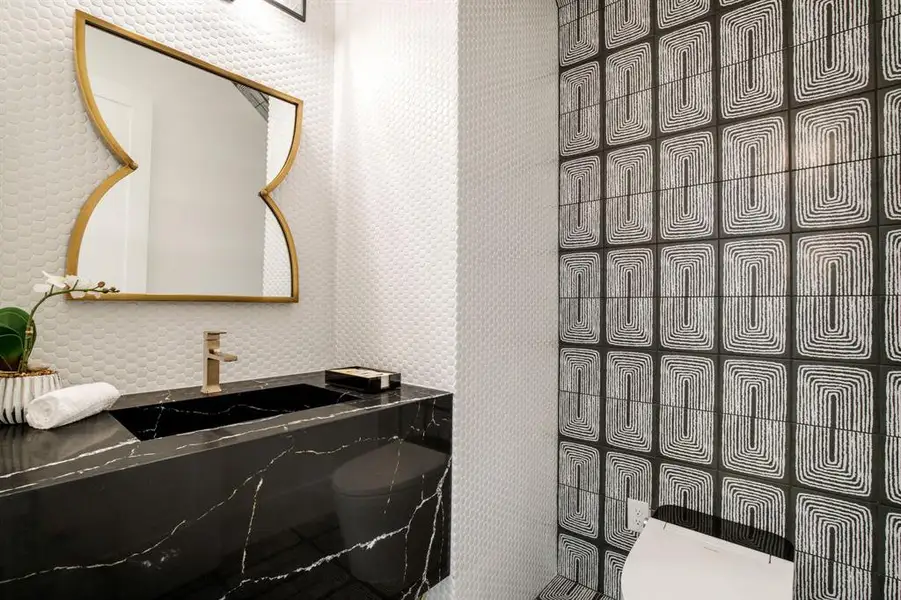 Powder room featuring a sleek black vanity with integrated sink, gold-toned faucet, and a decorative gold-framed mirror Powder room featuring a sleek black vanity with integrated sink, gold-toned faucet, and a decorative gold-framed mirror