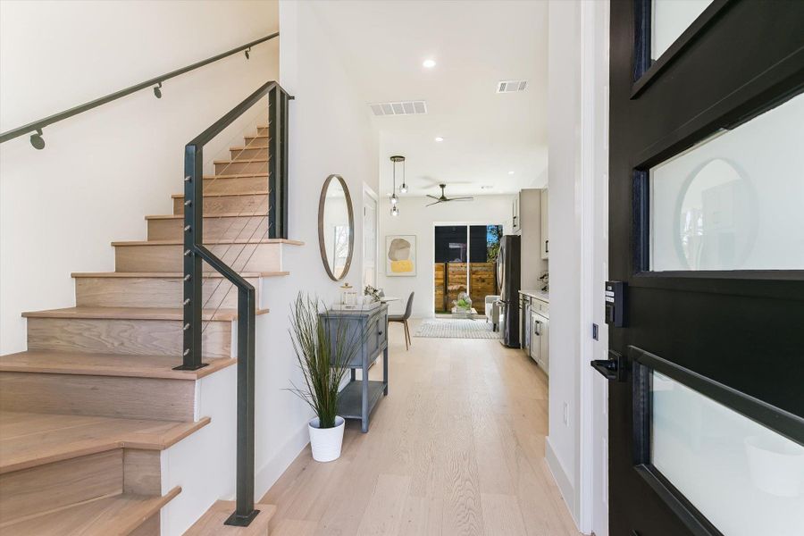 The ultimate open-concept layout. Looking from the entryway toward the living area, you can see how the light oak floors and high ceilings create an airy, expansive feel that connects the kitchen, dining, and outdoor spaces.