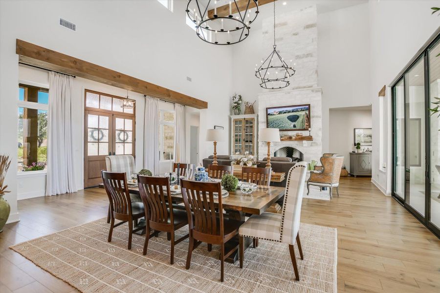 Dining room with a chandelier, a high ceiling, light wood-style floors, and a fireplace Dining room with a chandelier, a high ceiling, light wood-style floors, and a fireplace