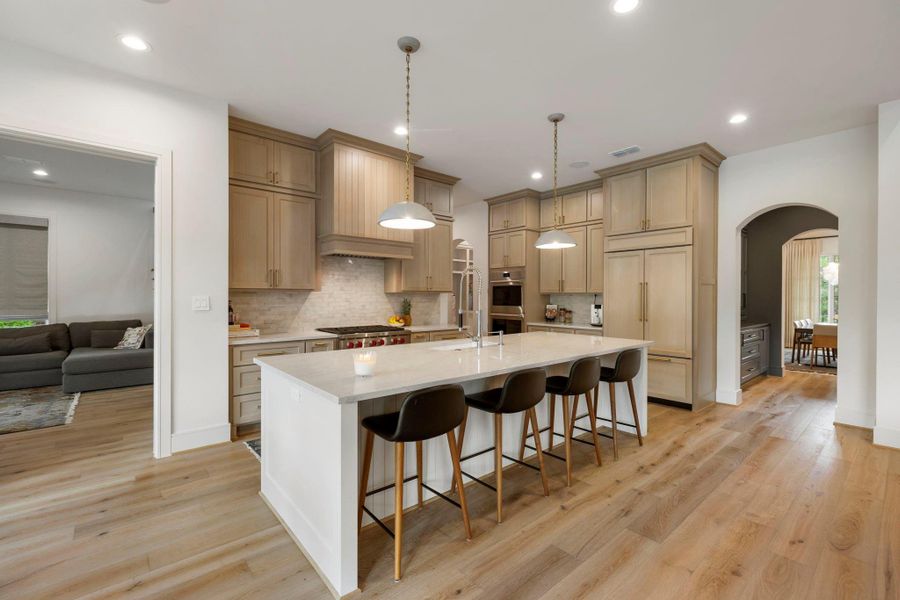 Chef’s kitchen with custom cabinetry, a large marble island with seating, Wolf appliances and a Sub-Zero built-in refrigerator, and elegant pendant lighting—designed for both everyday living and effortless entertaining.