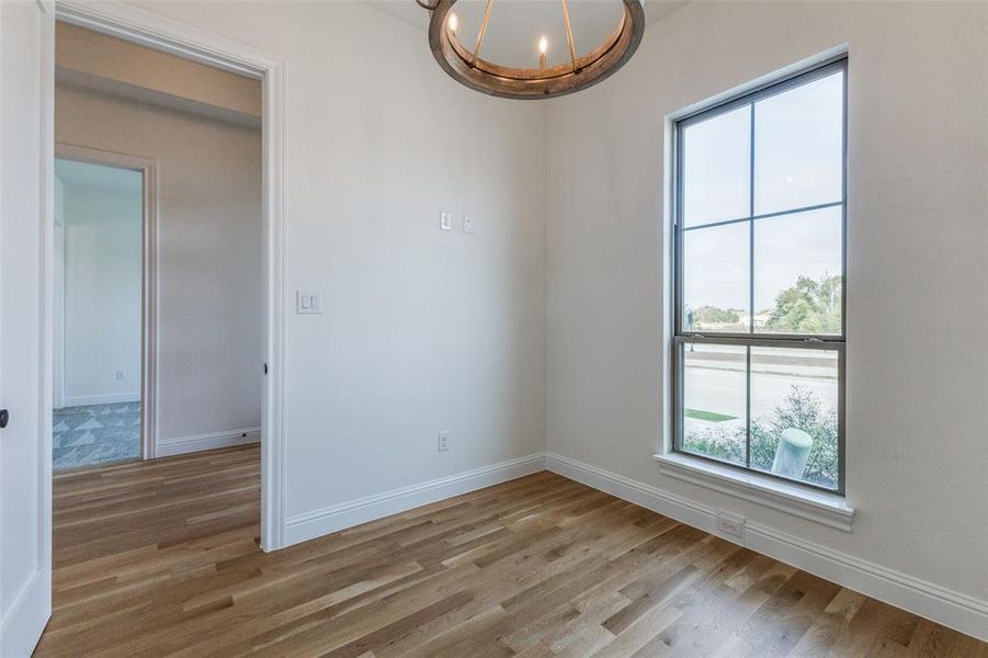 Empty room with wood finished floors, a chandelier, and baseboards