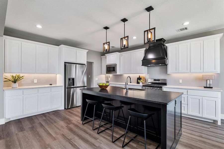 Kitchen featuring hardwood / wood-style floors, custom exhaust hood, sink, a center island with sink, and stainless steel appliances