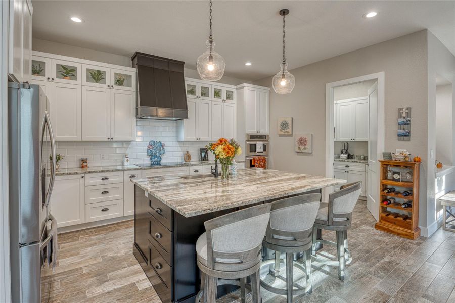 Kitchen with a breakfast bar area, white cabinetry, backsplash, light stone countertops, and custom range hood