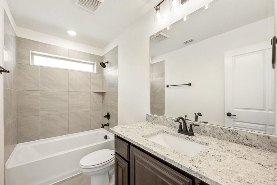 Bathroom with granite countertop vanity, tiled tub-shower combo, and dark hardware fixtures