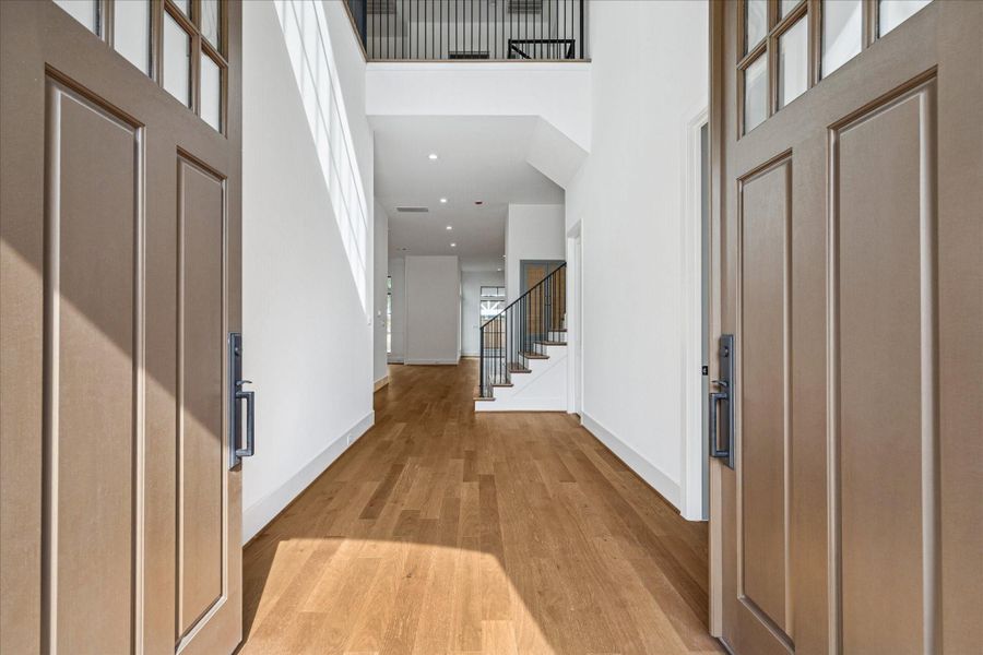 A soaring two-story foyer welcomes you with natural light, expansive sightlines, and the level of architectural detail that defines Arch Angelo Homes. Wide-plank hardwood floors flow throughout, complemented by an elegant staircase featuring iron balusters and oak treads. The arched double front doors create a dramatic entrance, while the upper gallery landing adds volume and visual interest. Thoughtful millwork, clean lines, and balanced proportions establish a timeless entry experience. A soaring two-story foyer welcomes you with natural light, expansive sightlines, and the level of architectural detail that defines Arch Angelo Homes. Wide-plank hardwood floors flow throughout, complemented by an elegant staircase featuring iron balusters and oak treads. The arched double front doors create a dramatic entrance, while the upper gallery landing adds volume and visual interest. Thoughtful millwork, clean lines, and balanced proportions establish a timeless entry experience.