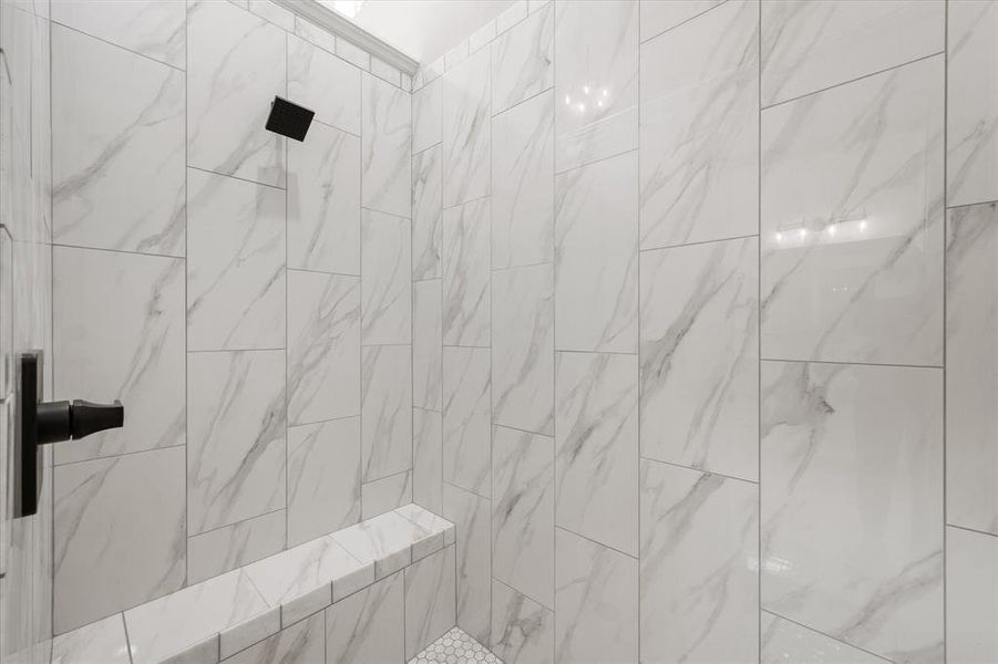Shower enclosure featuring floor-to-ceiling white marble-look tile, a built-in bench, matte black showerhead, and matte black lever handle