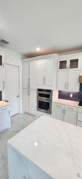 Kitchen with glass insert cabinets, white cabinets, light stone counters, and recessed lighting Kitchen with glass insert cabinets, white cabinets, light stone counters, and recessed lighting