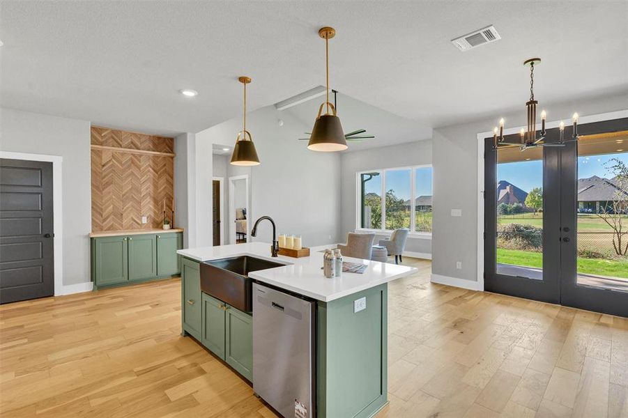 Kitchen with green cabinets, light wood finished floors, stainless steel dishwasher, a kitchen island with sink, and pendant lighting Kitchen with green cabinets, light wood finished floors, stainless steel dishwasher, a kitchen island with sink, and pendant lighting
