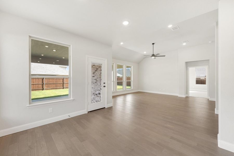 Open living area with hardwood floors, vaulted ceiling, ceiling fan, and backyard-facing windows and door.