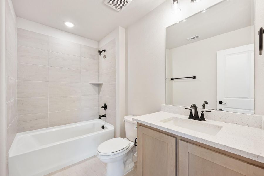 Bathroom with tiled tub and shower, single vanity with quartz countertop, and dark bronze fixtures