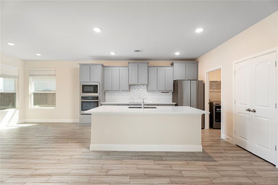 Kitchen featuring gray cabinetry, a kitchen island with sink, light countertops, oven, and recessed lighting