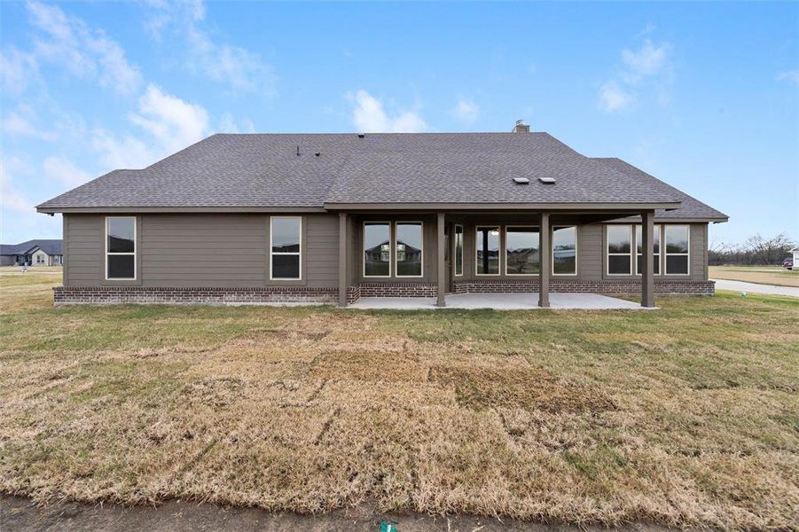 Back of house featuring roof with shingles, a lawn, a patio area, brick siding, and a chimney Back of house featuring roof with shingles, a lawn, a patio area, brick siding, and a chimney