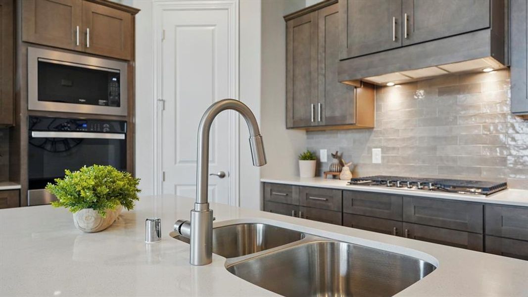 Kitchen island featuring a double basin stainless steel sink with a high-arch faucet, light-toned countertops, and built-in stainless steel appliances