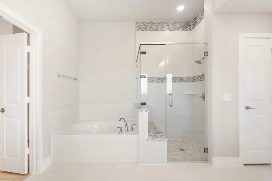 Bathroom with soaking tub, glass-enclosed shower, white tile walls, and mosaic accent border