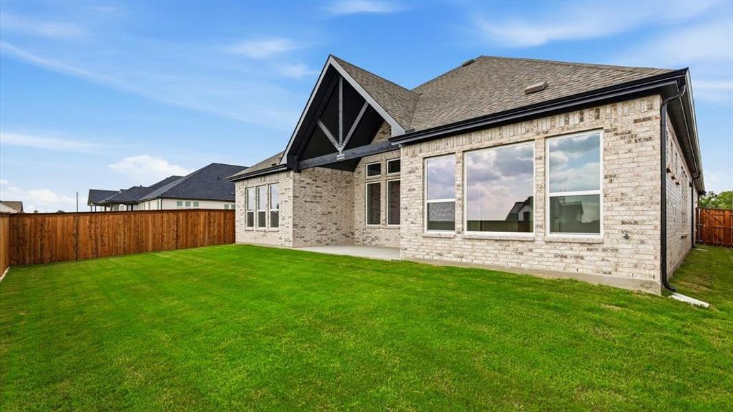 Spacious backyard featuring a manicured lawn, full privacy fencing, and a covered patio area