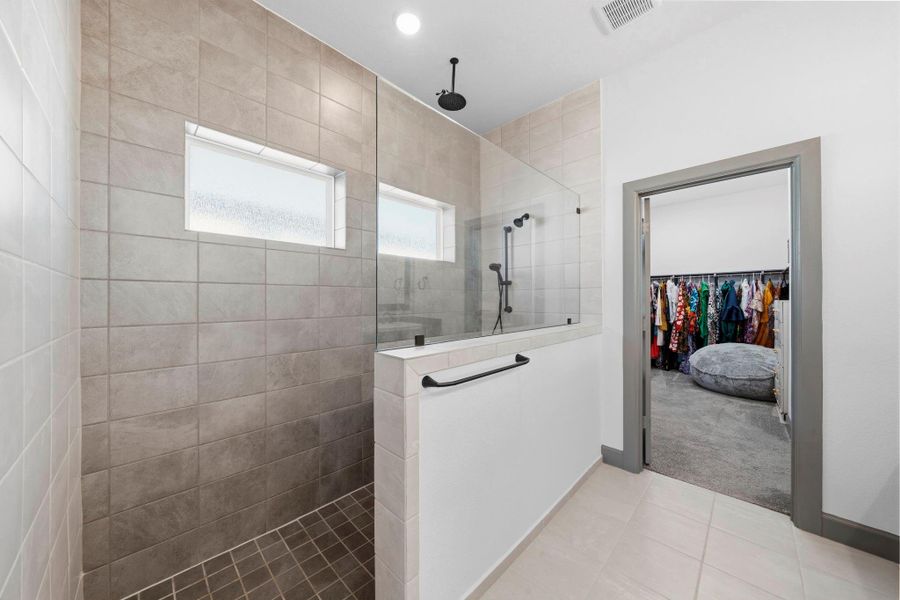 Spa-inspired primary bathroom featuring dual vanities with granite countertops, oversized mirrors, and modern lighting, complemented by a walk-in shower with sleek tile surround and direct access to a spacious walk-in closet.