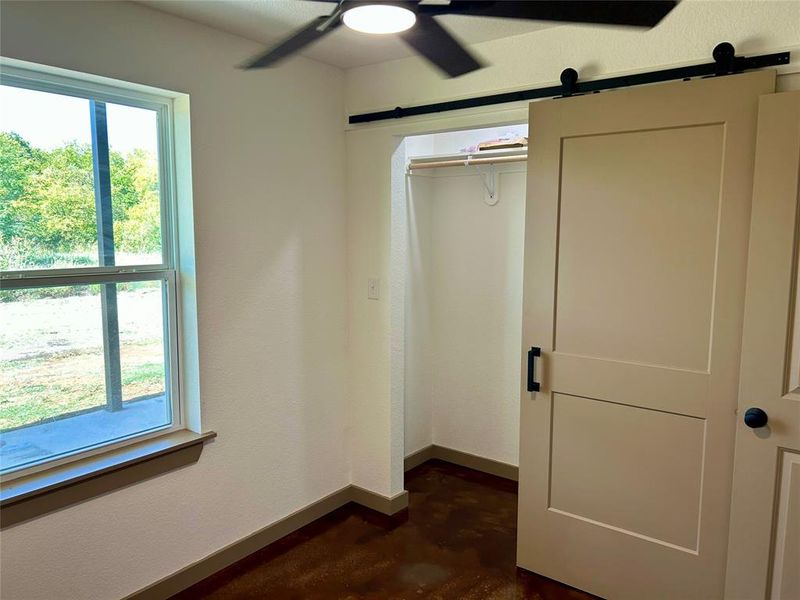 Unfurnished bedroom featuring multiple windows, ceiling fan, concrete floors, and a closet