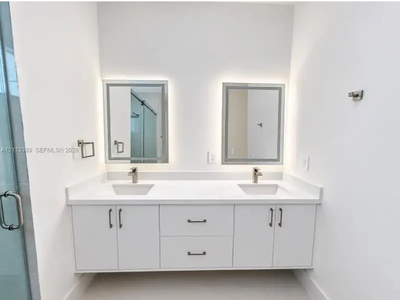 Floating double vanity featuring a white countertop with dual undermount sinks, satin-finish faucets, built-in lower cabinetry, and two rectangular LED-backlit mirrors