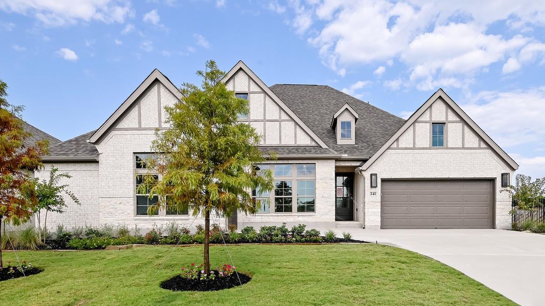 Tudor house featuring a shingled roof, brick siding, concrete driveway, and a front yard