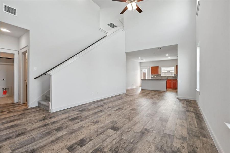 Unfurnished living room with stairway, a ceiling fan, a towering ceiling, dark wood-type flooring, and recessed lighting Unfurnished living room with stairway, a ceiling fan, a towering ceiling, dark wood-type flooring, and recessed lighting