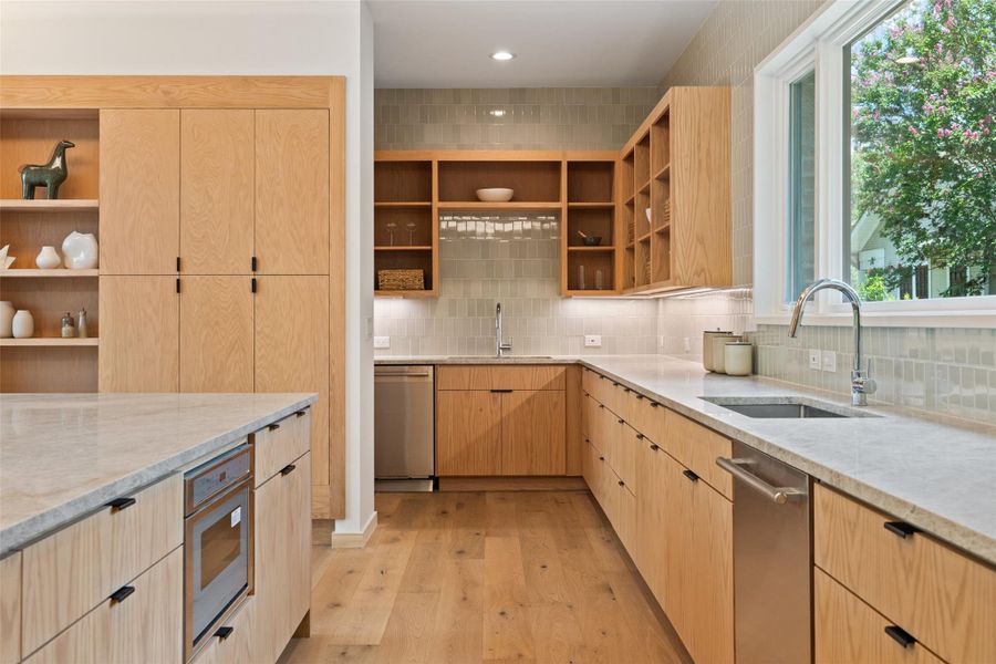 Kitchen with light brown cabinets, light stone counters, backsplash, light wood-type flooring, and open shelves